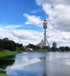 Olympiapark in München mit Olympiastadion und Olympiaturm, umgeben von Grünflächen und dem Olympiasee.