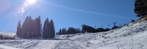 Schneebedeckte Piste in Lenggries Brauneck mit einem Sessellift und strahlend blauem Himmel.